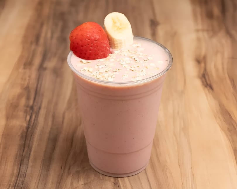 Strawberry banana smoothie in a clear cup, topped with oats, a strawberry, and a banana slice.